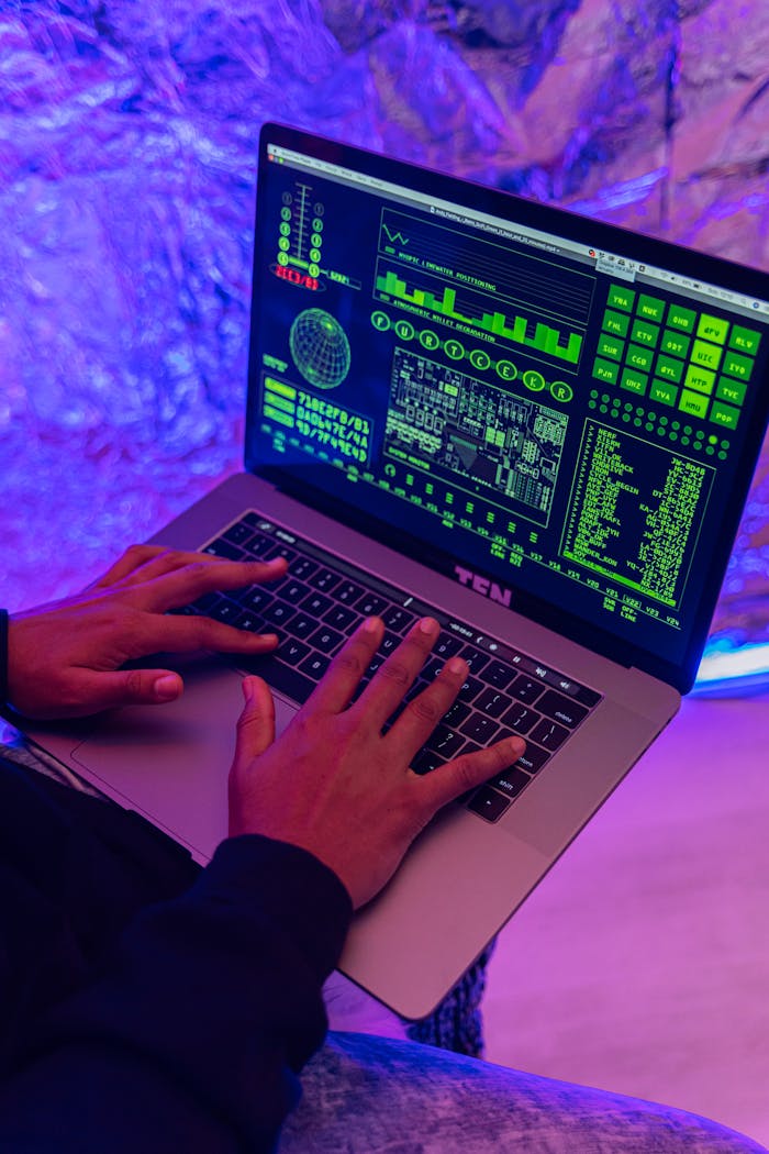 Services Close-up of hands typing on a laptop displaying green code, indoors, purple lighting.